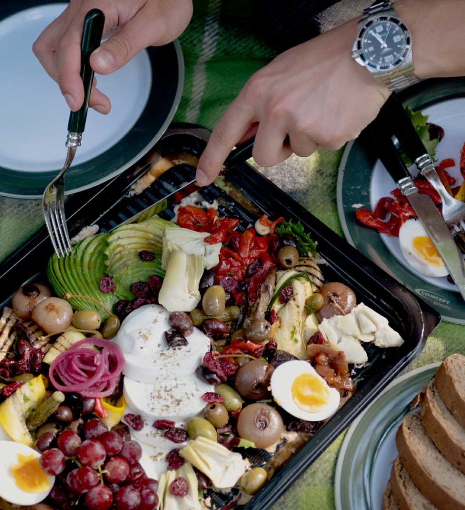 A pair of hands holding cutlery cut into a vegetarian platter laid out on a picnic blanket at Back of Beyond.