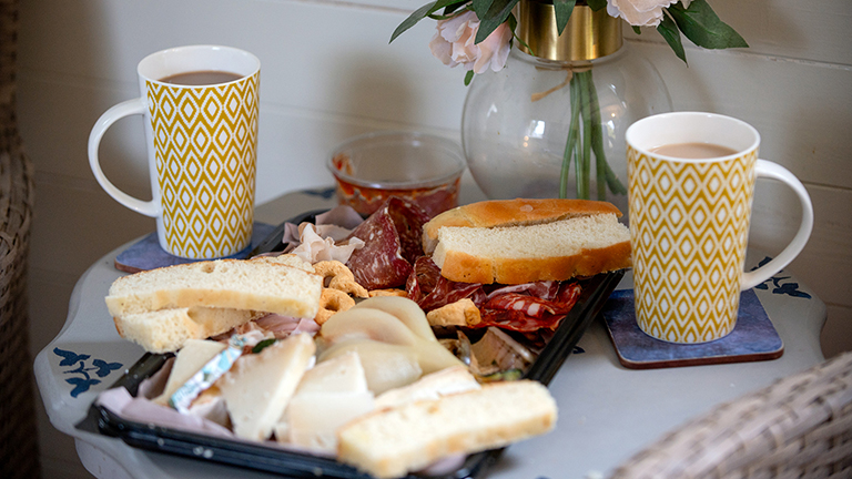 A charcuterie platter with two cups of tea in a glamping unit