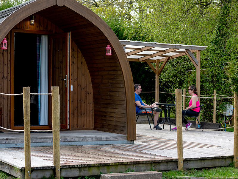 Couple sit on decking area of a glamping pod