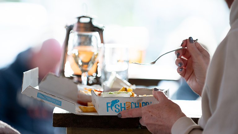 Person eating fish and chips at Back of Beyond Touring Park