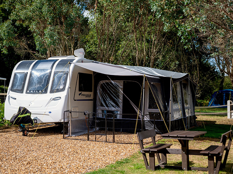 A large, fully serviced hardstanding pitch with caravan, awning and picnic bench.