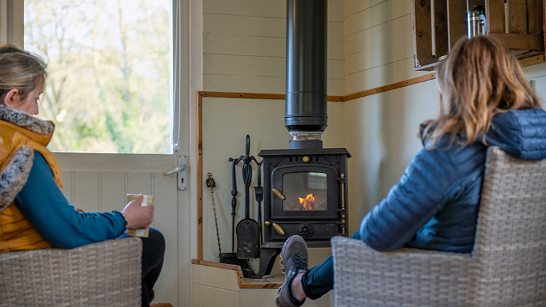Two people sat in front of a log fire in a shepherd hut.